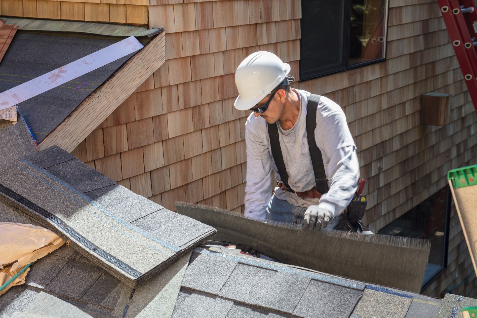 Man is engaged in a roofing replacement in Papillion, NE, installing asphalt roof shingles
