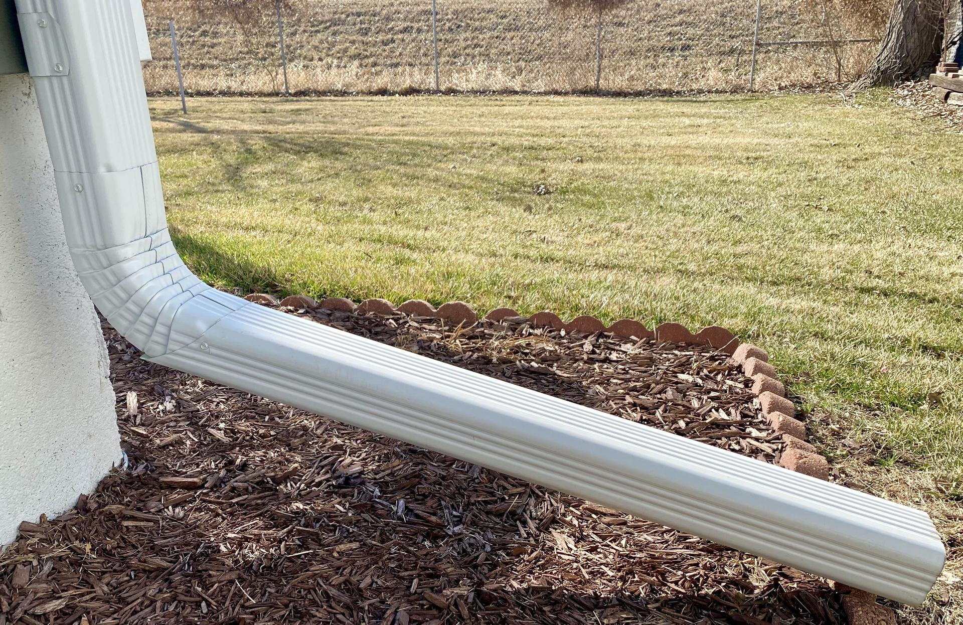 A white gutter is sitting on the side of a house next to a lawn | Siefken Roofing and Remodeling Services in Omaha, NE