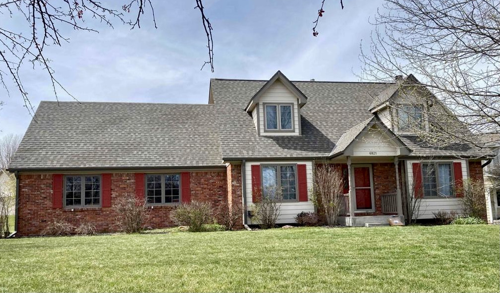 A large brick house with a gray roof and red shutters  | Roofing Projects | Siefken Roofing and Remodeling Services in Omaha, NE