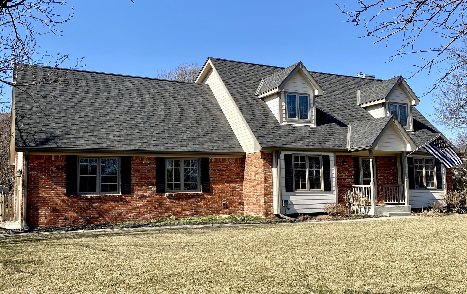 A large brick house with a gray roof and black shutters | Siefken Roofing and Remodeling Services in Omaha, NE