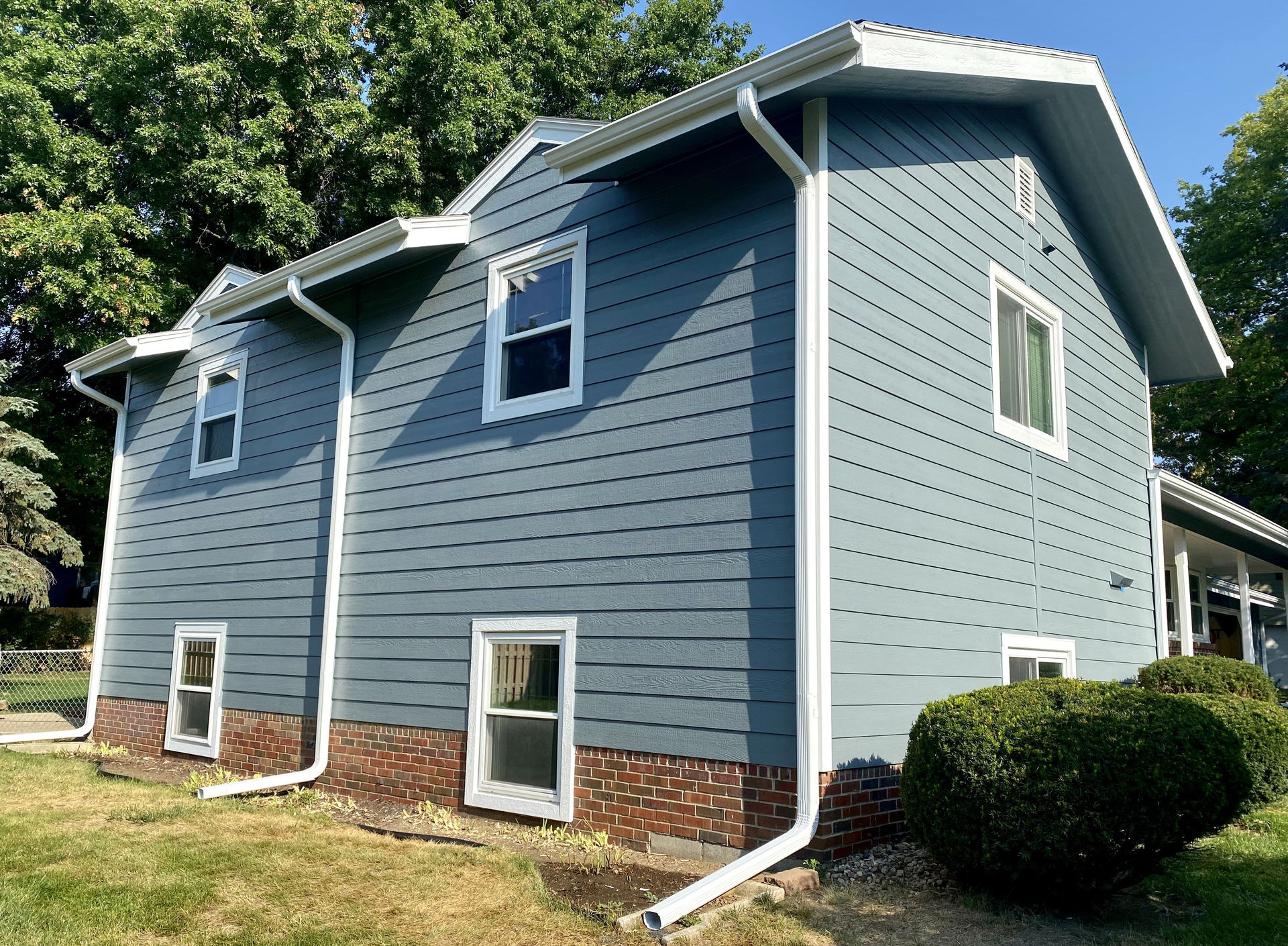 A blue house with white siding and gutters is sitting on top of a lush green field  | Gutters Projects | Siefken Roofing and Remodeling Services in Omaha, NE