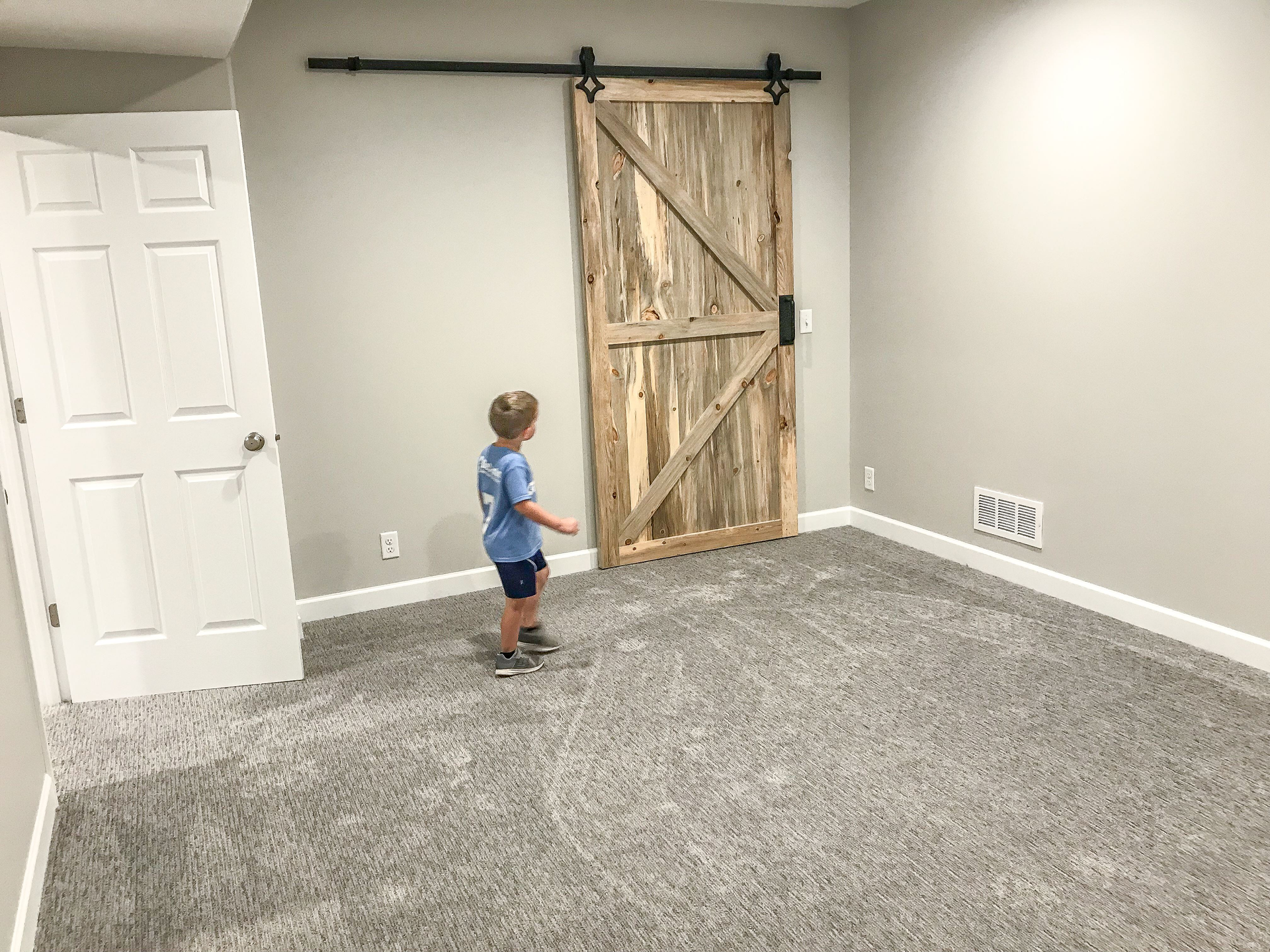 A young boy is standing in an empty room with a sliding barn door | Kitchen Projects | Siefken Roofing and Remodeling Services in Omaha, NE