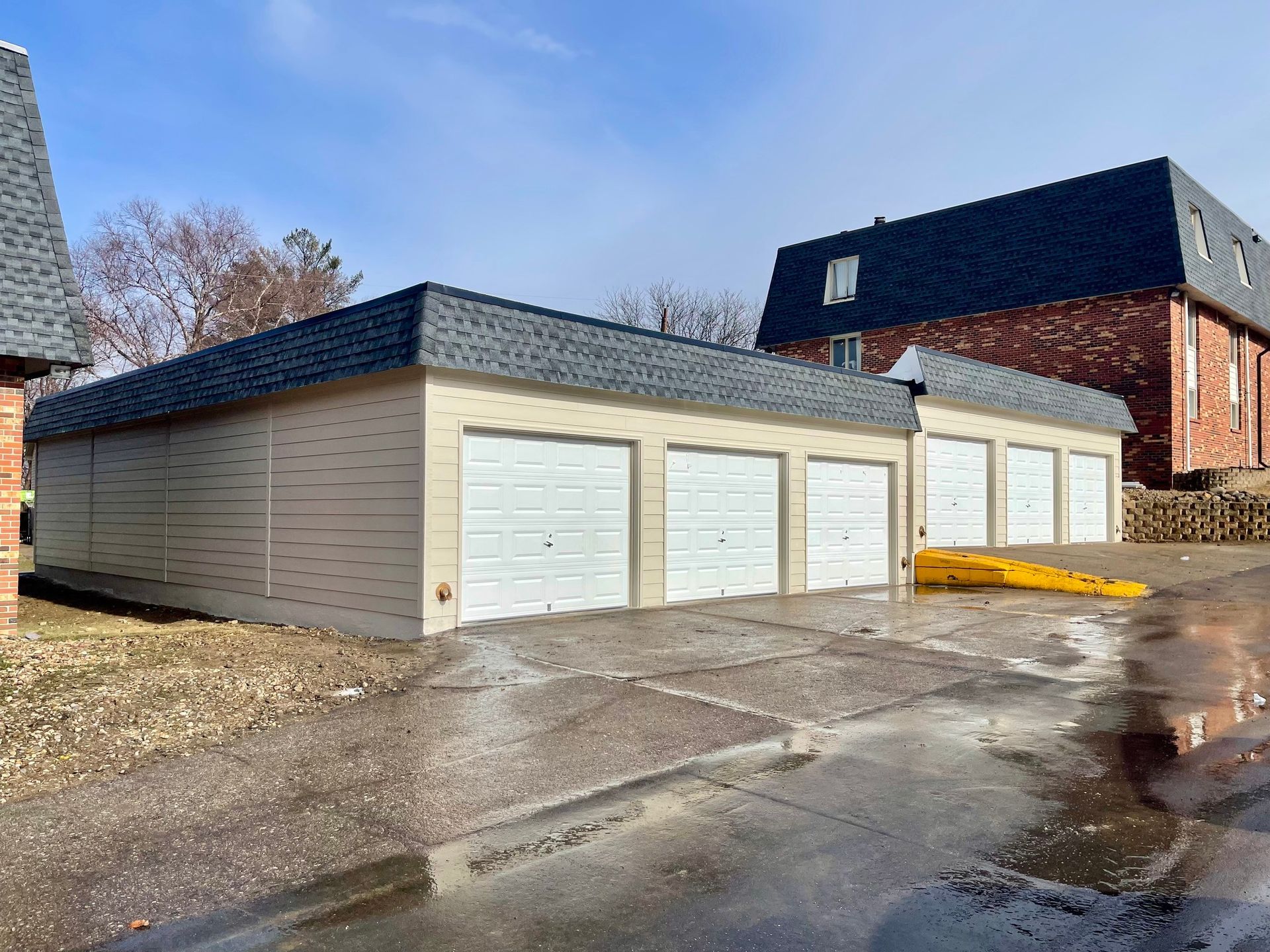 A row of garages with white doors and a brick building in the background | Fire Restoration Projects | Siefken Roofing and Remodeling Services in Omaha, NE