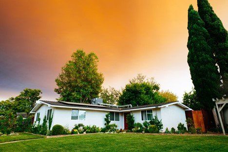 A white house with a lush green lawn in front of a cloudy sky | Siefken Roofing and Remodeling Services in Omaha, NE