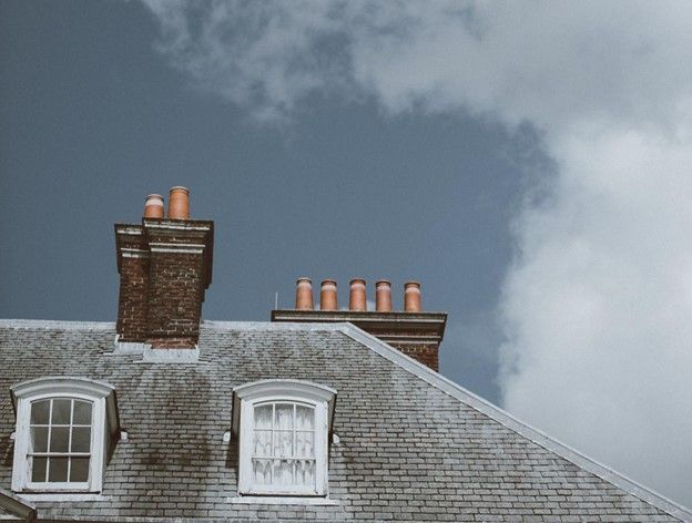 A brick building with chimneys on the roof and a blue sky in the background | Siefken Roofing and Remodeling Services in Omaha, NE