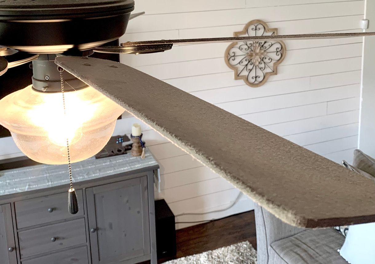 Ceiling fan with light fixture in a room with a wooden wall and a cabinet.