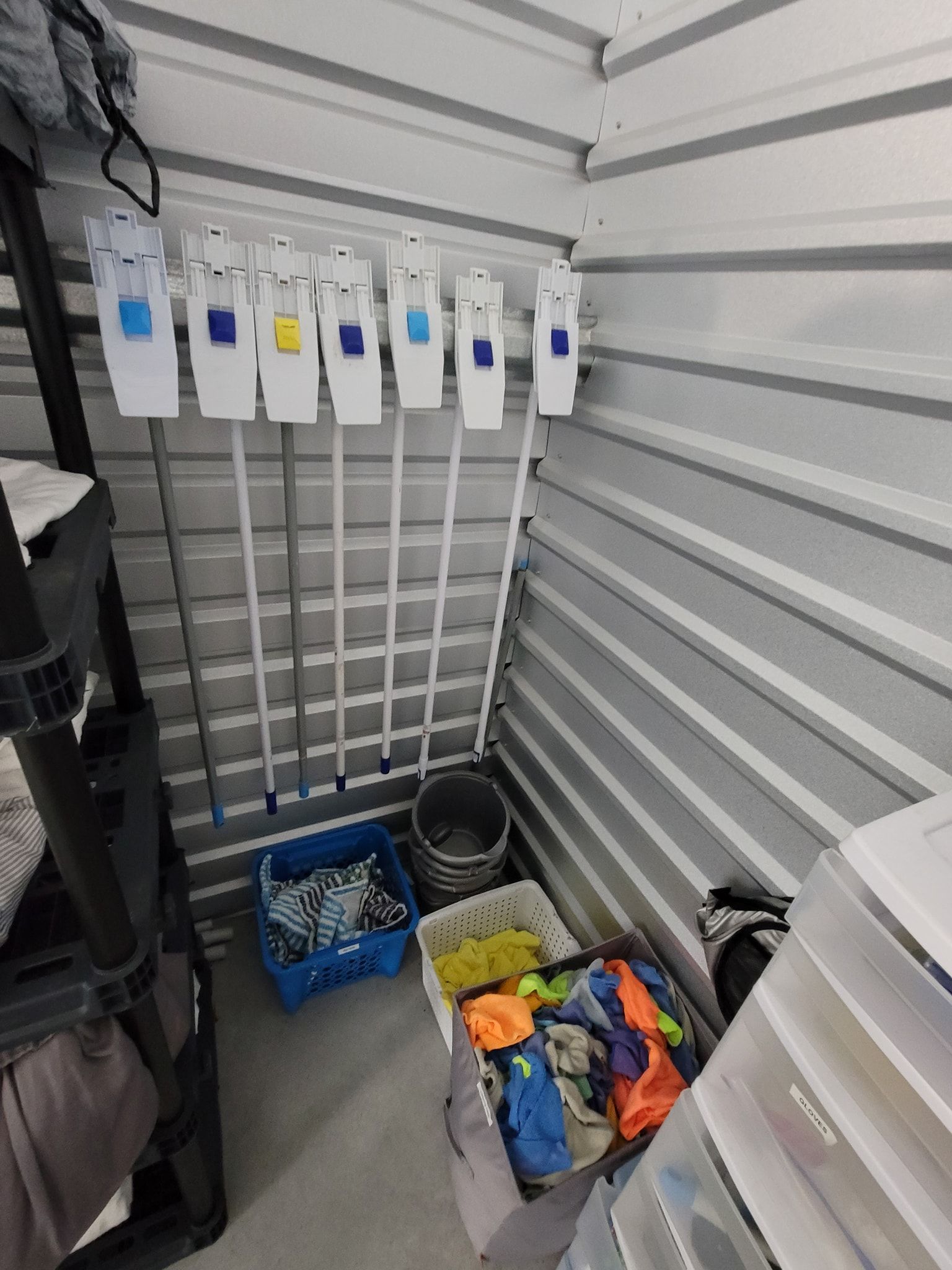 Storage unit interior with cleaning supplies and containers; mops hanging.
