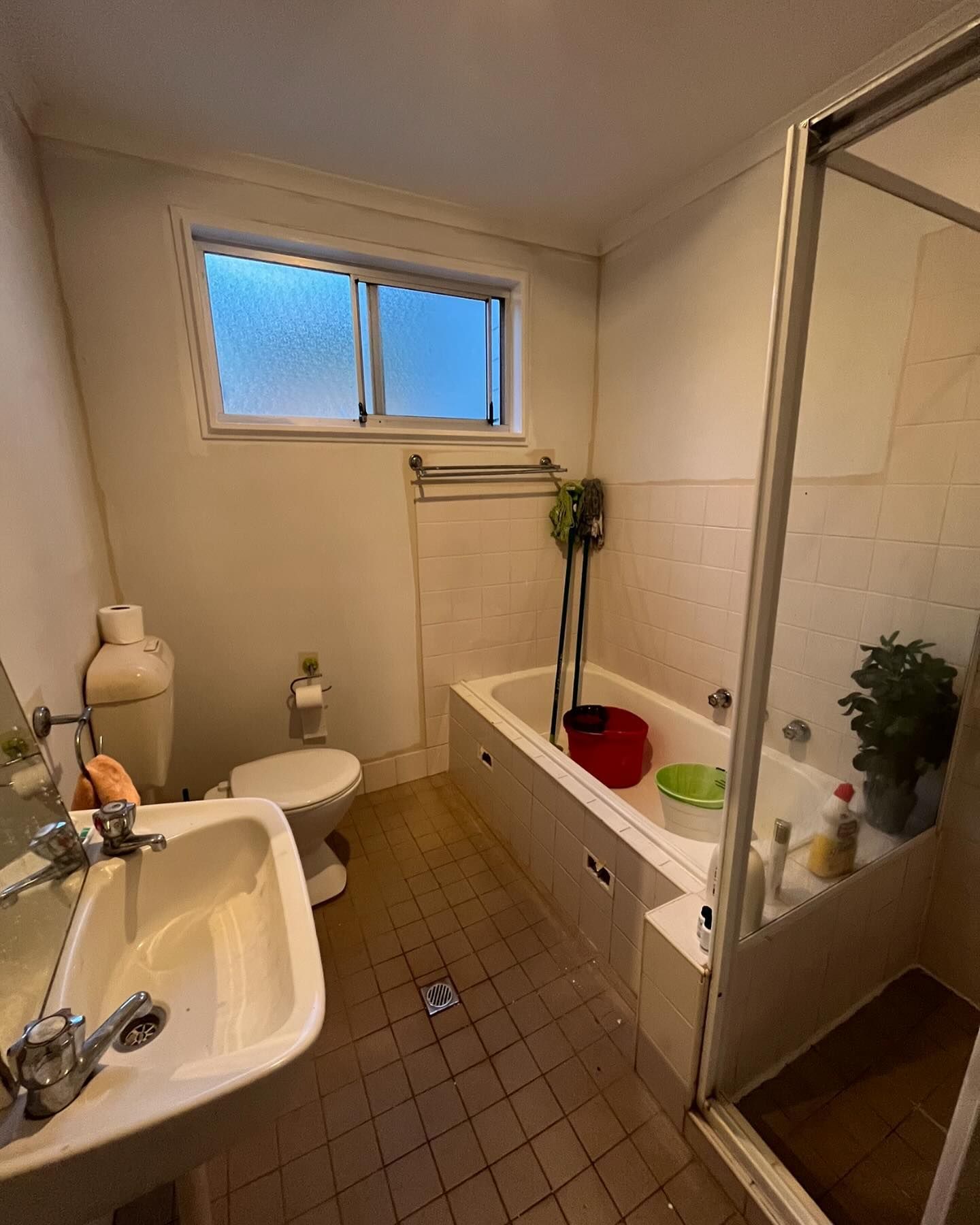 A Dated, White Bathroom With a Pedestal Sink, Toilet, Window, Tiled Floors — Coastbuilt Building Services in Thrumster, NSW