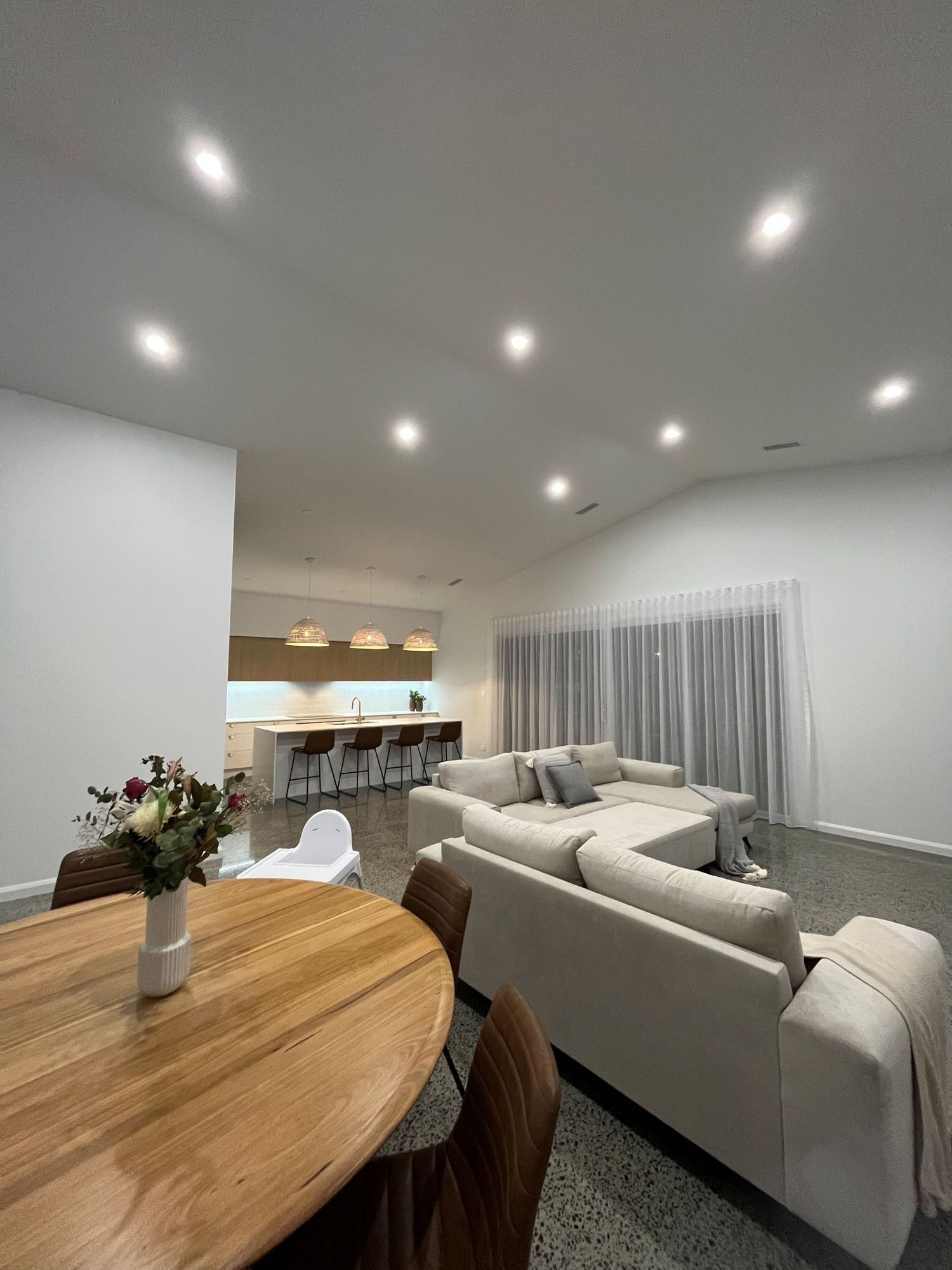 A Bright, Open-plan Living Room With a Round Wooden Dining Table — Coastbuilt Building Services in Thrumster, NSW