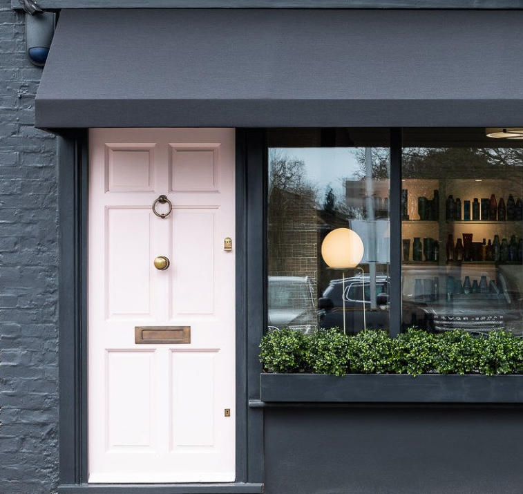 A store front with a pink door and a black awning