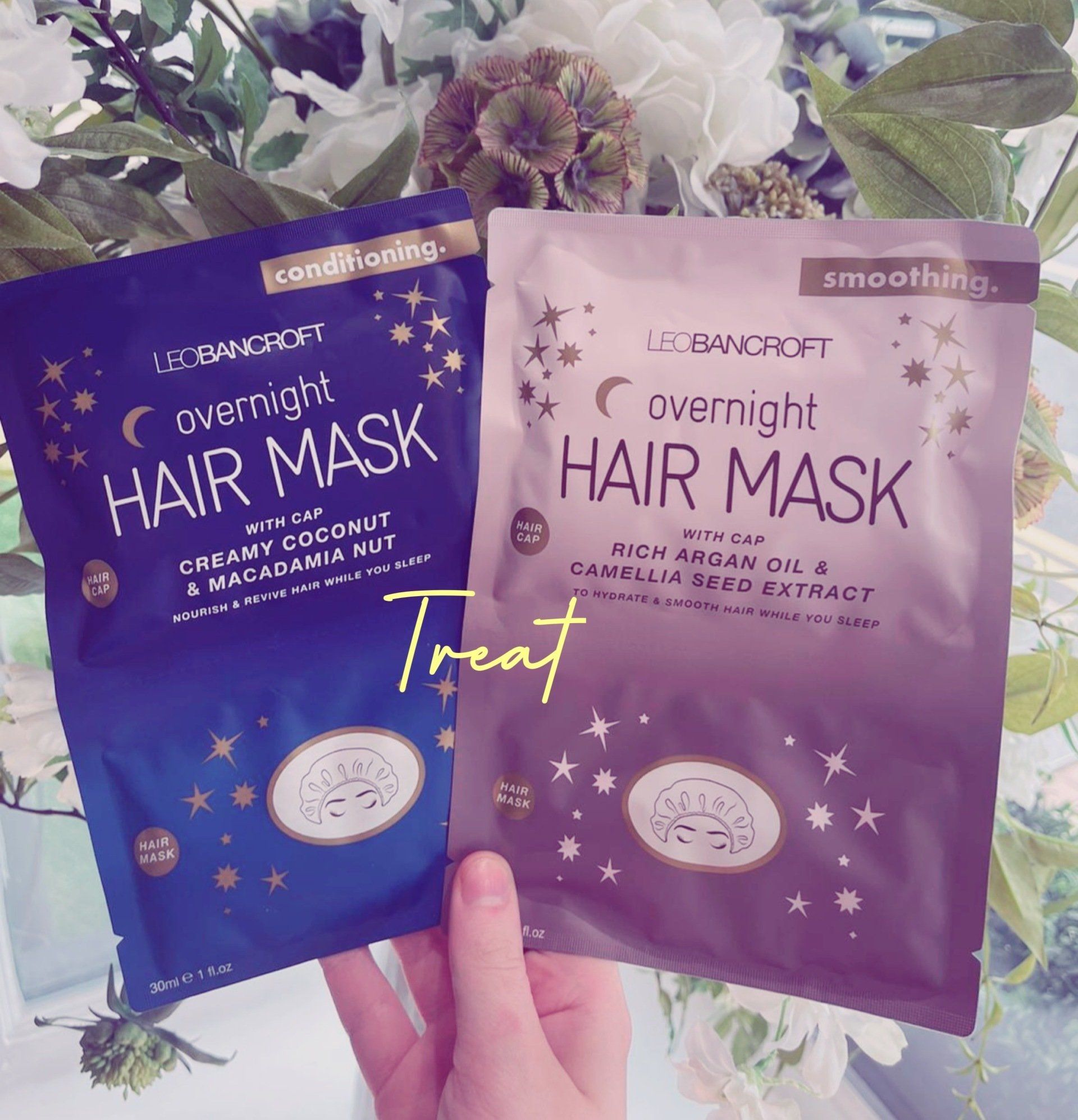 Two purple overnight hair mask packets held in hand, labeled “treat,” on a floral background