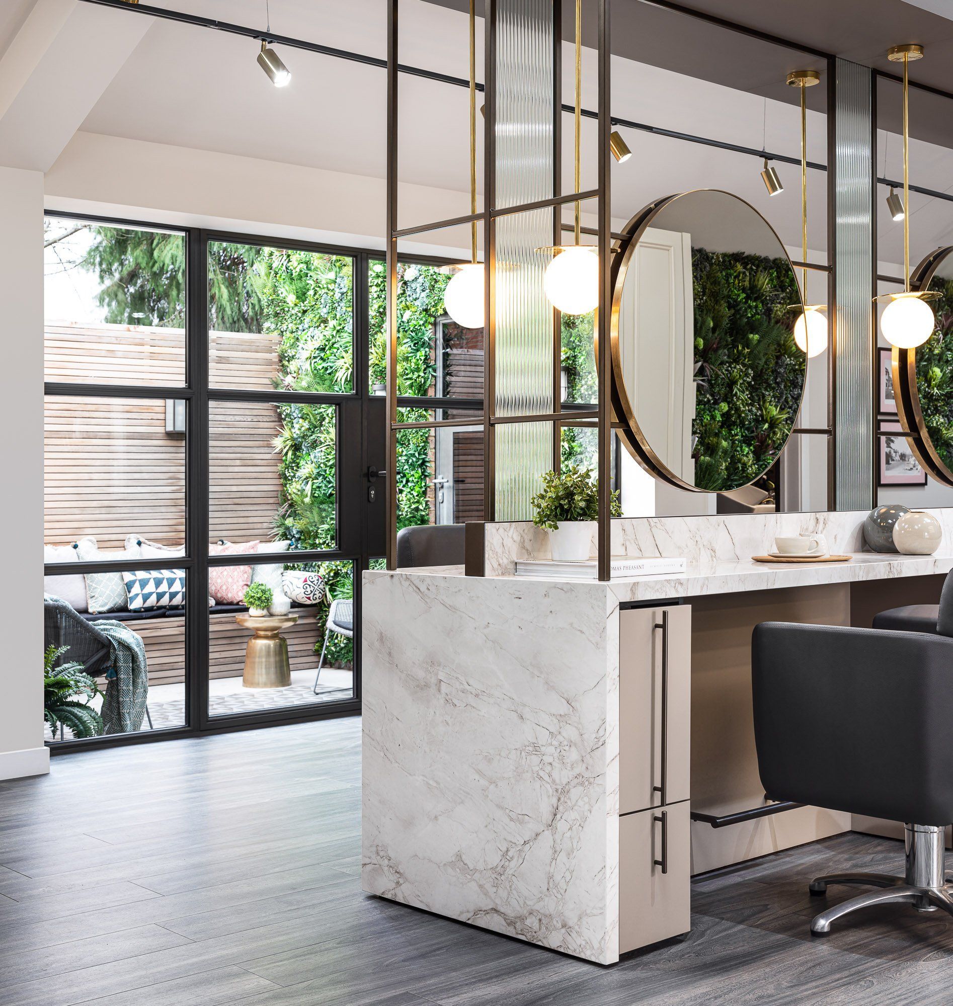 Leo Bancroft Modern salon interior with marble styling stations, round mirrors, and black chairs by large windows