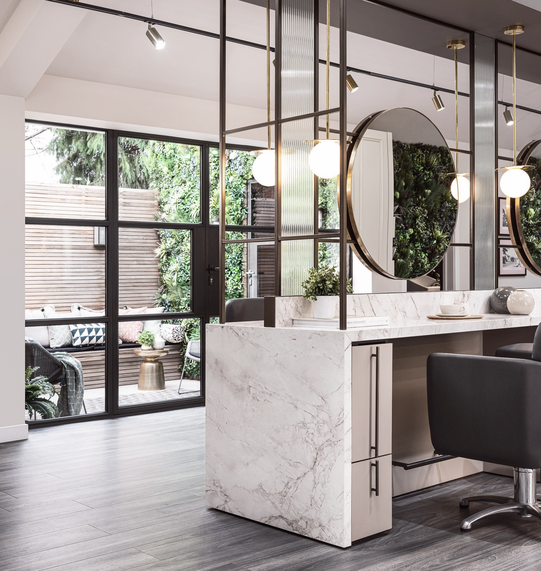 Leo Bancroft Modern salon interior with marble styling stations, round mirrors, and black chairs by large windows