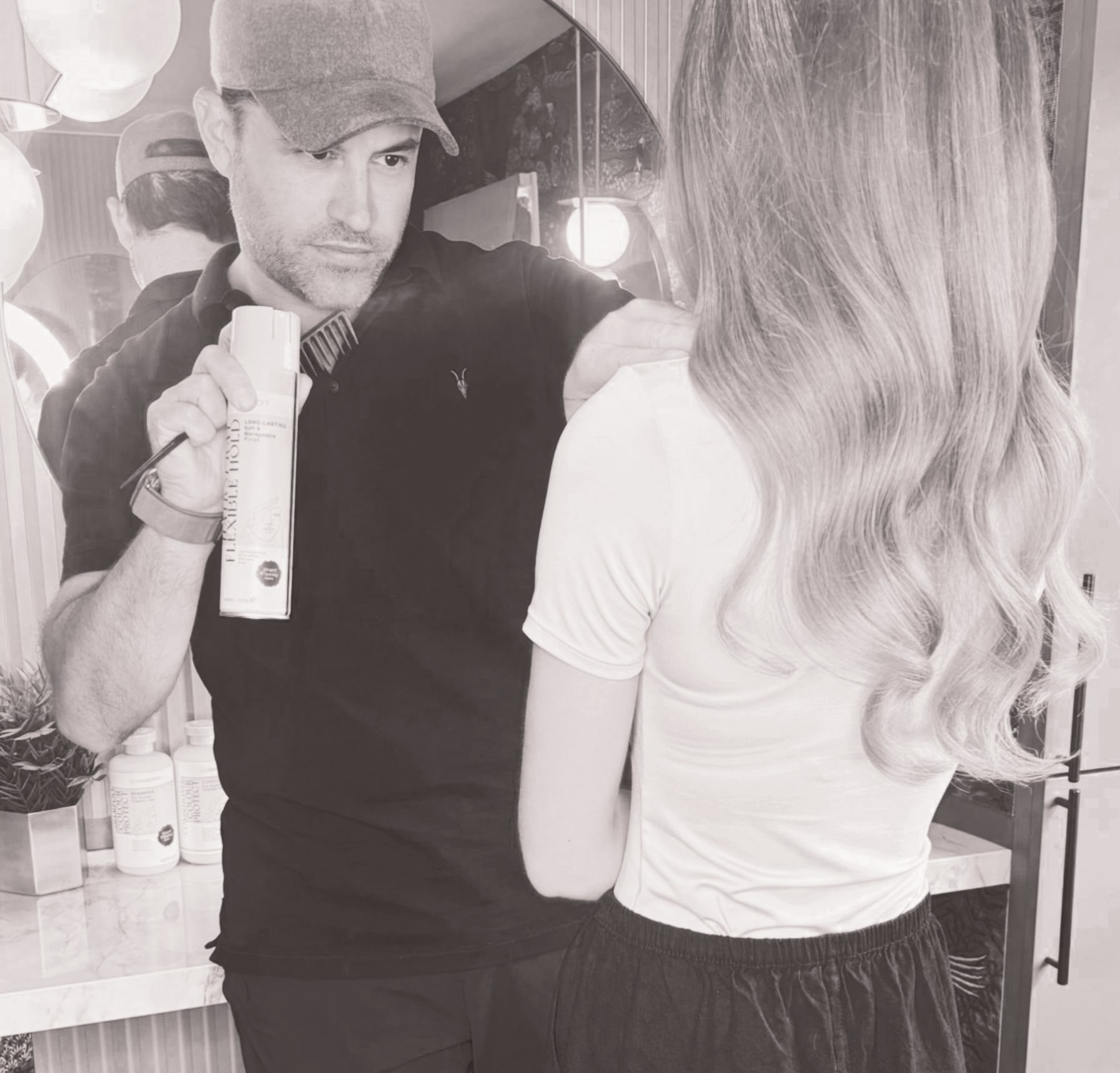 Leo Bancroft curling a client’s hair at a salon mirror, with another woman reflected in the background