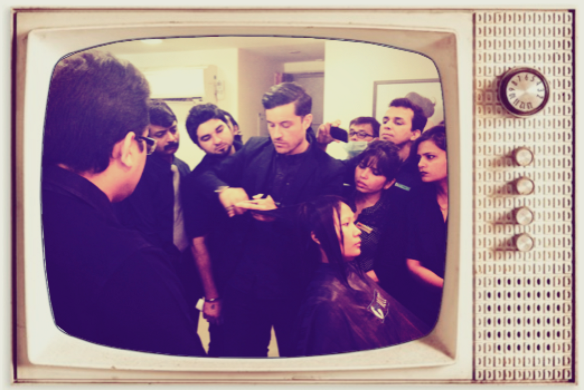 People gathered around a man speaking in a retro TV frame, with a vintage sepia tone.