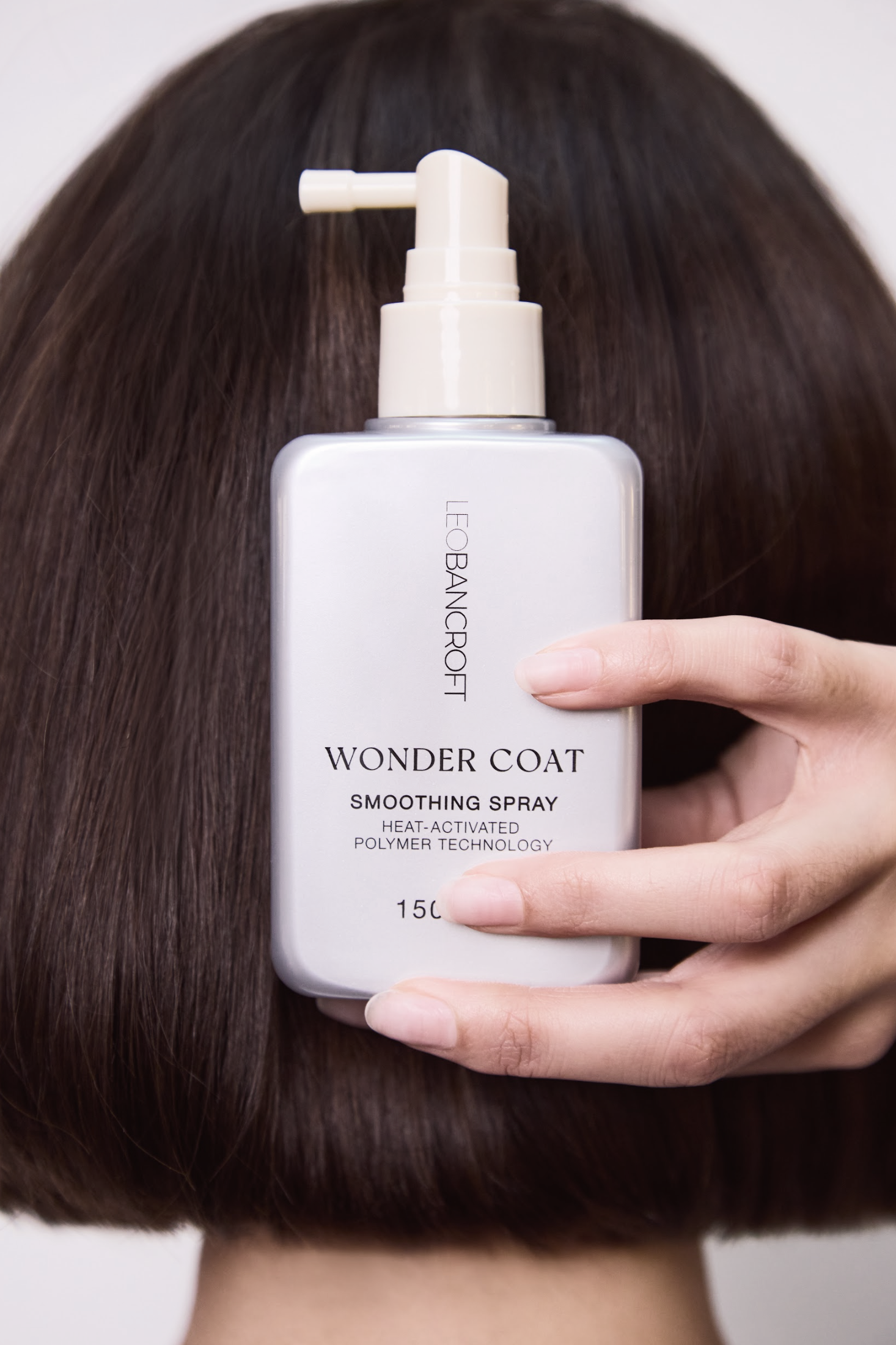 Hand holding a Leo Bancroft hair product bottle in front of short dark brown hair