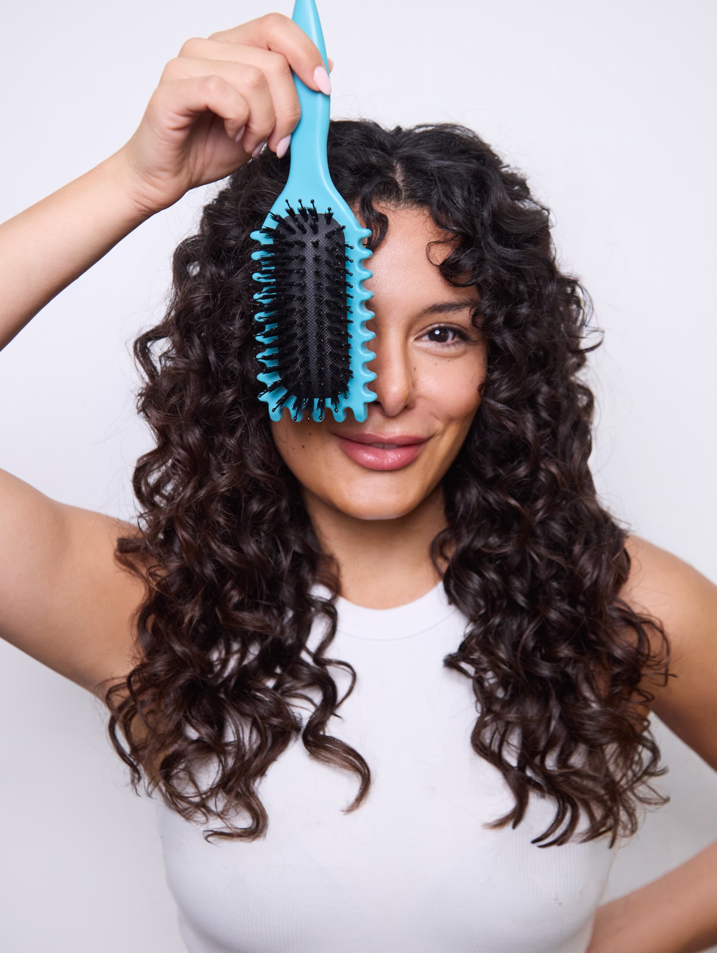Leo Bancroft model Woman with curly hair holding a turquoise hairbrush over her face, wearing a white shirt