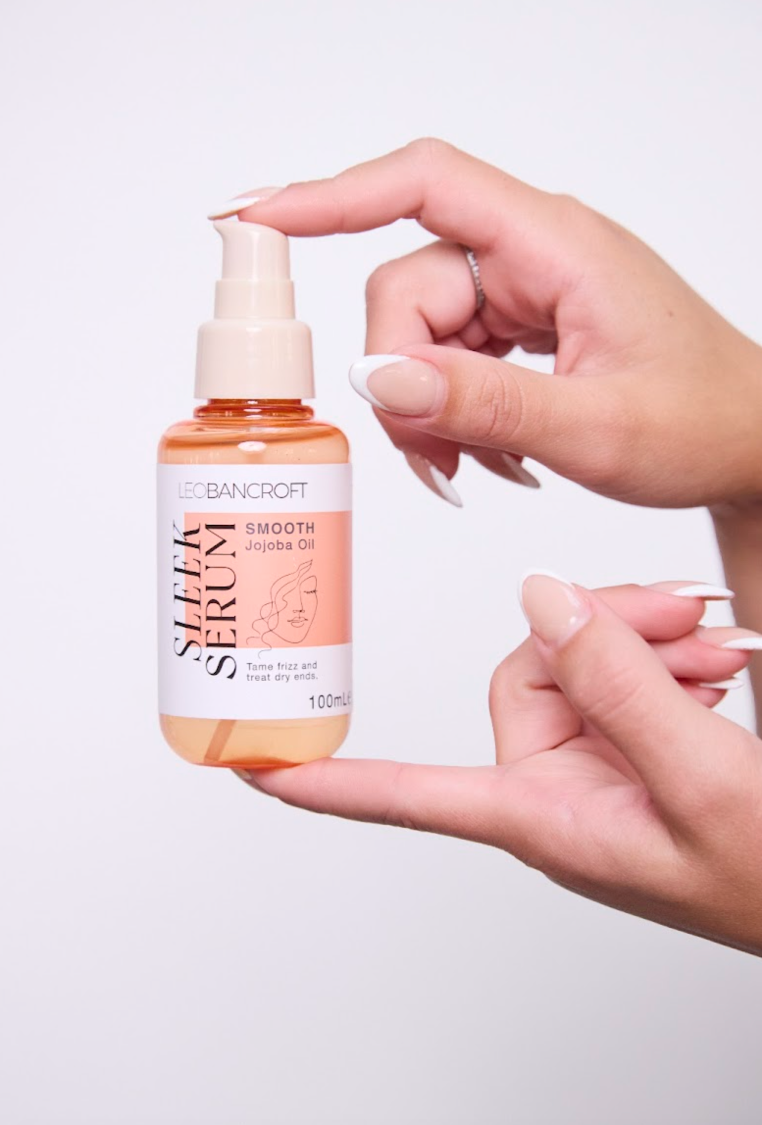 Leo Bancroft model Hands holding an orange pump bottle of skincare serum on a light background