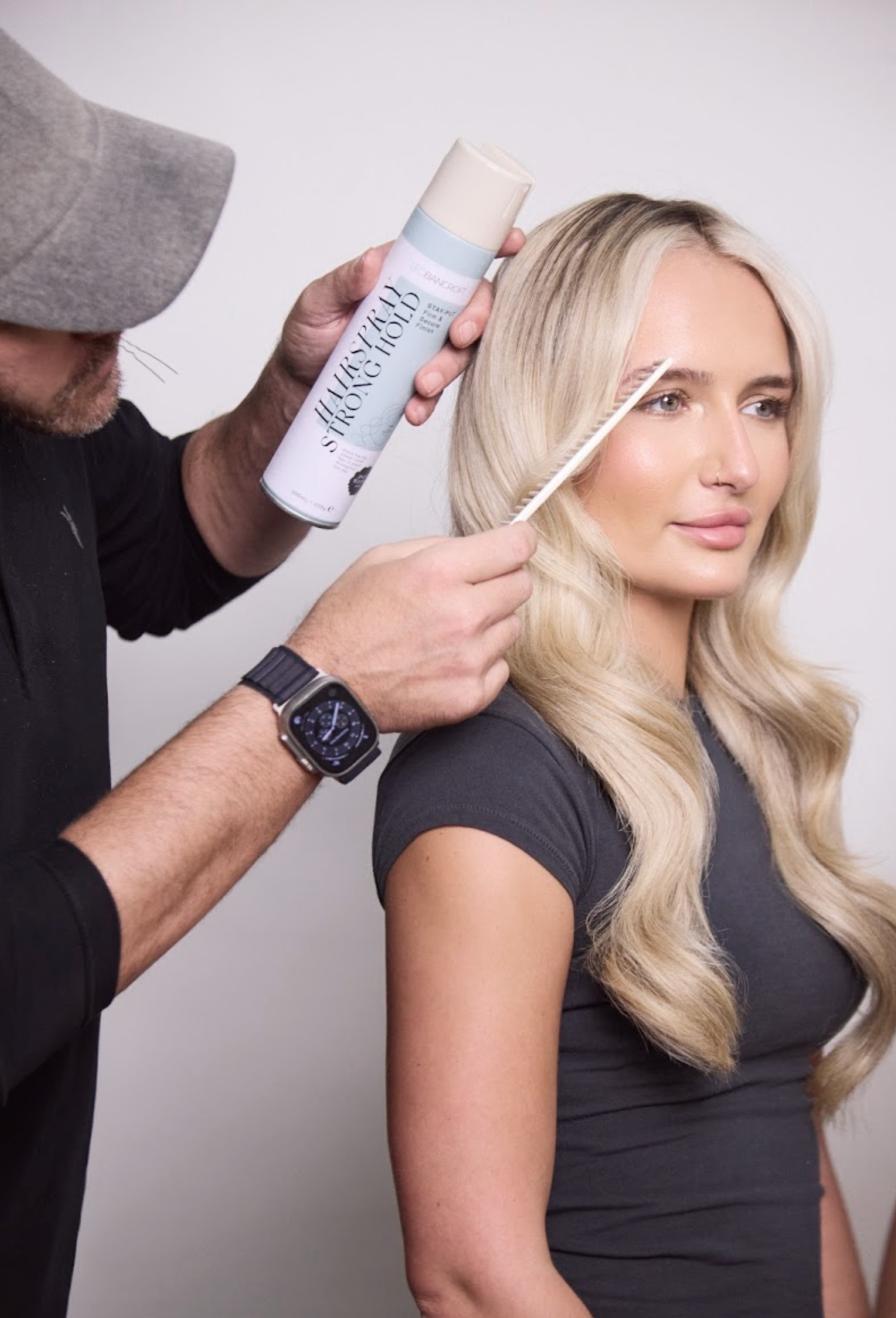 Leo Bancroft curling a blonde woman’s hair with a curling iron and spray in a salon setting