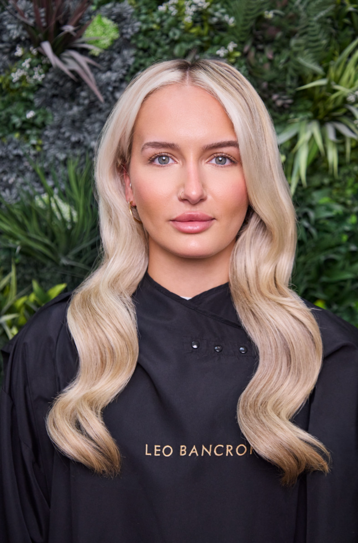 Blonde Leo Bancroft model in a black hoodie standing against a leafy green backdrop