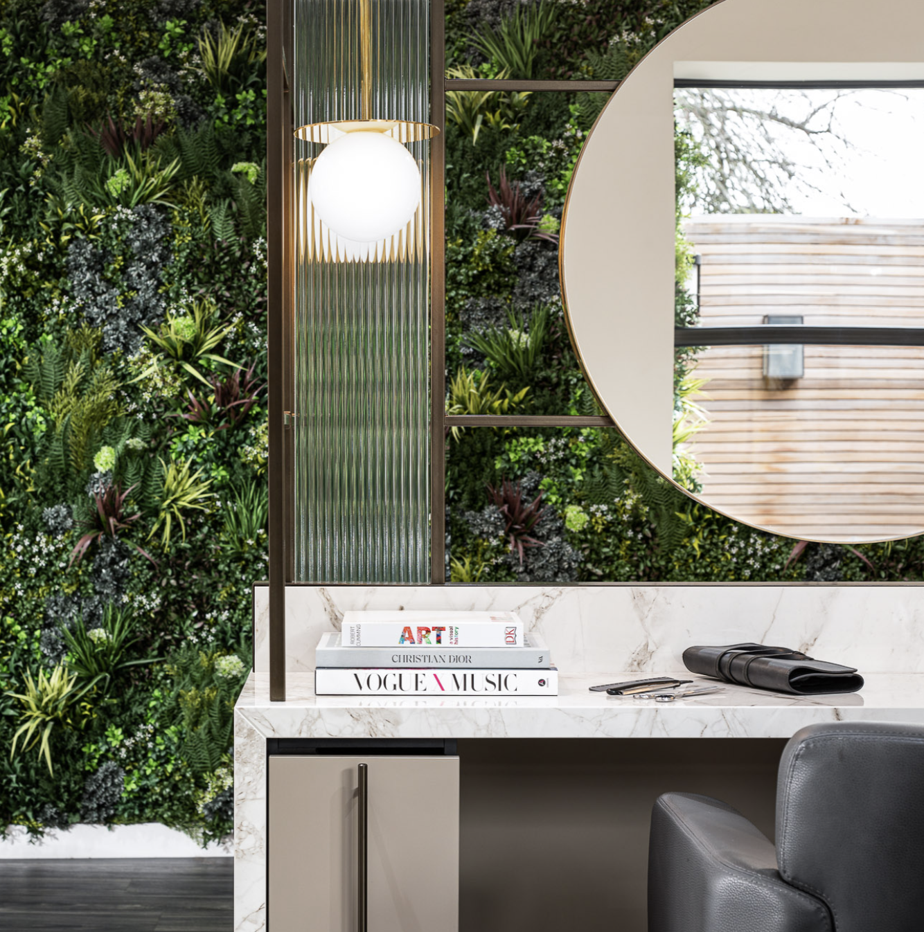 A room with a green wall , a desk , a chair and a mirror.
