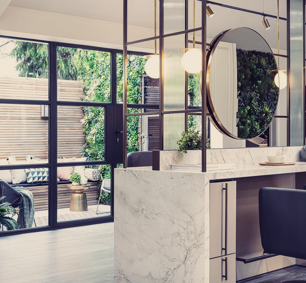 Modern marble reception desk in a bright lobby with round mirror and large windows overlooking greenery