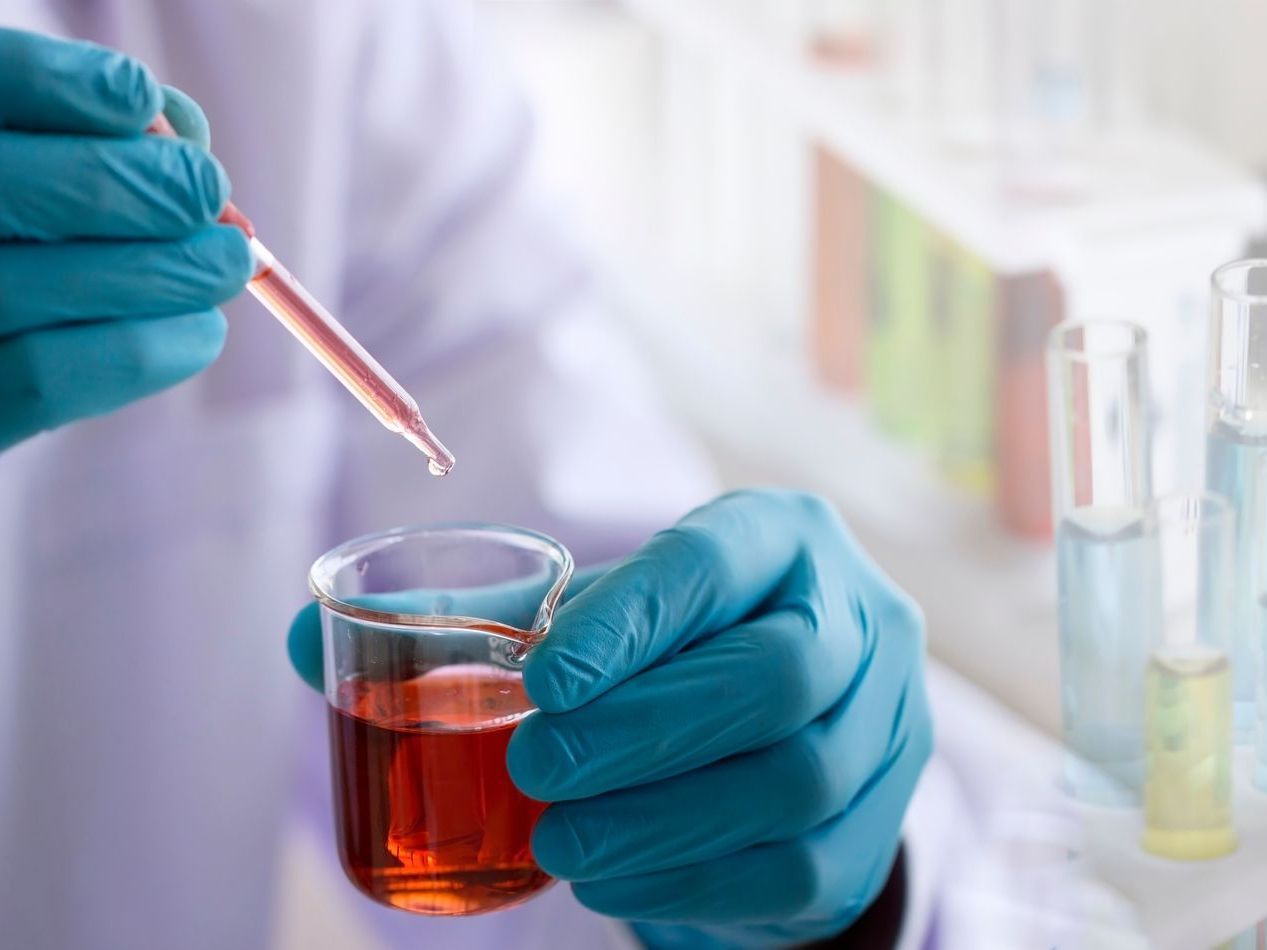 A scientist is pouring liquid into a beaker with a pipette.