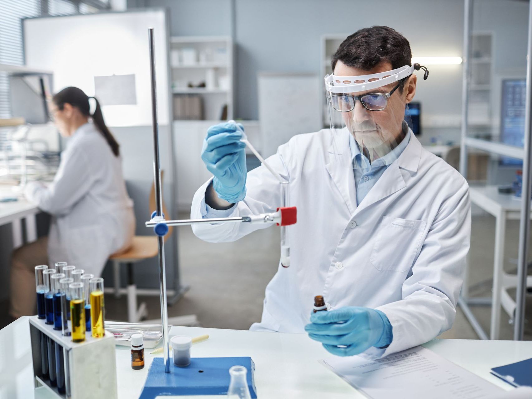 A scientist is working in a laboratory holding a test tube and a pipette.