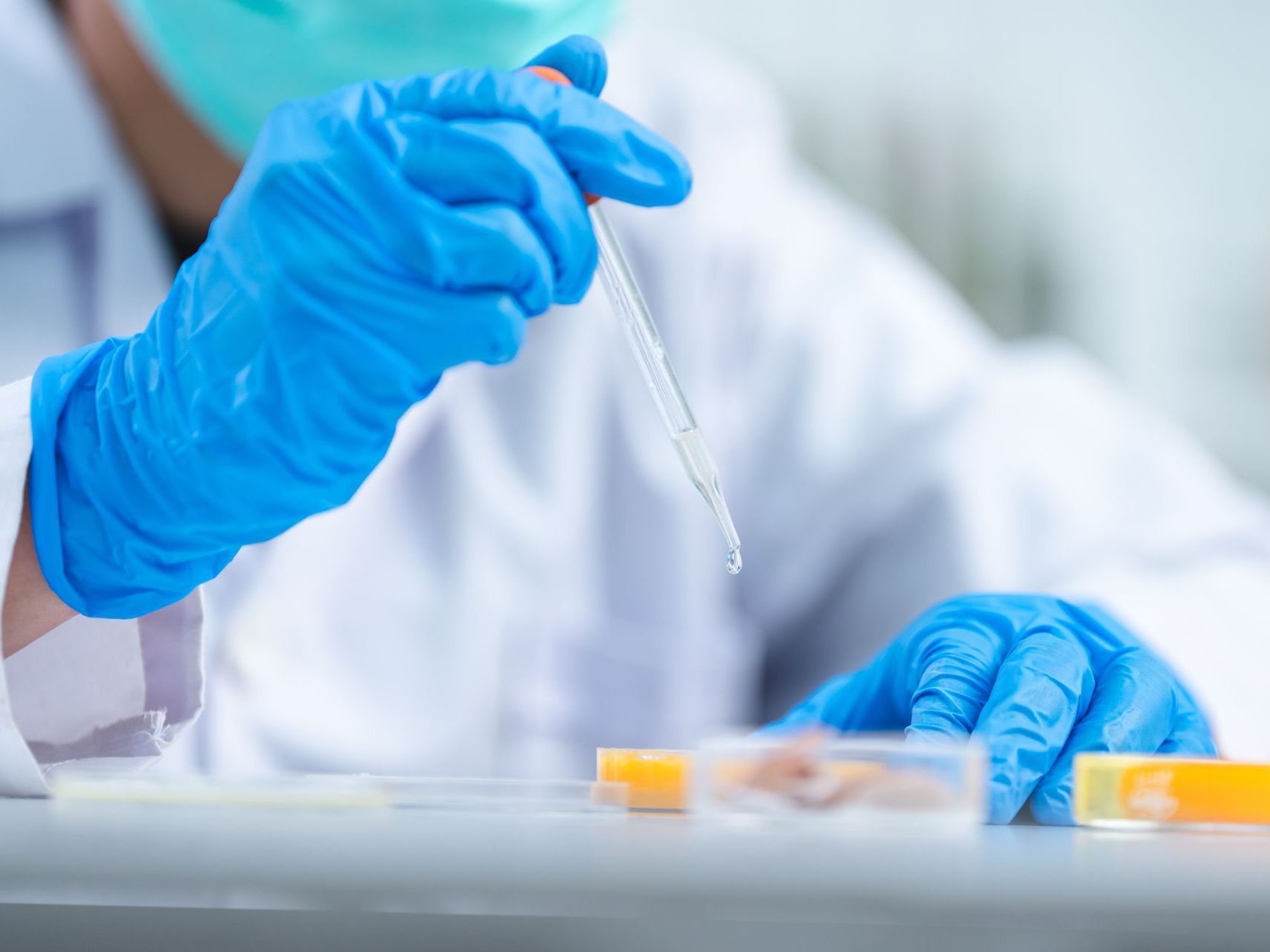 A scientist wearing a mask and blue gloves is holding a pipette.