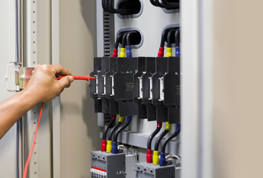 Hand using a red screwdriver to adjust electrical circuit breakers in a panel box