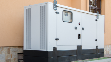 Large white industrial generator unit beside a building, with vents, access panels, and a small window.