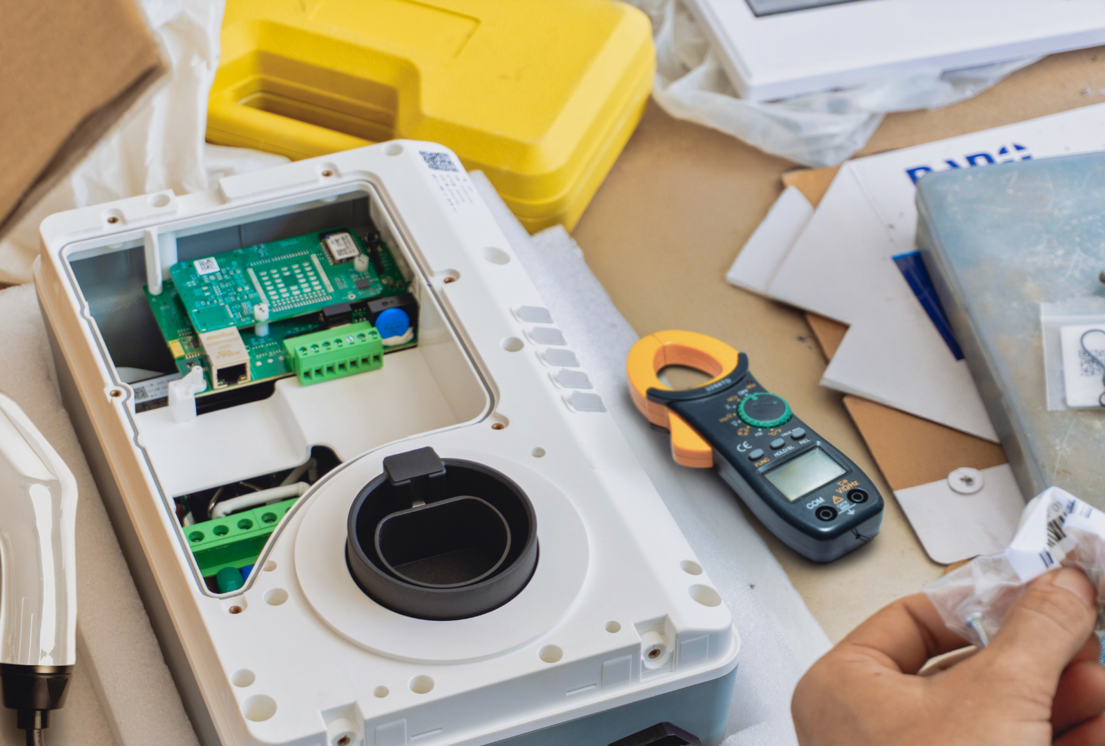 Electronics repair scene with open device, tools, circuit board, and a hand holding a small part on a workbench
