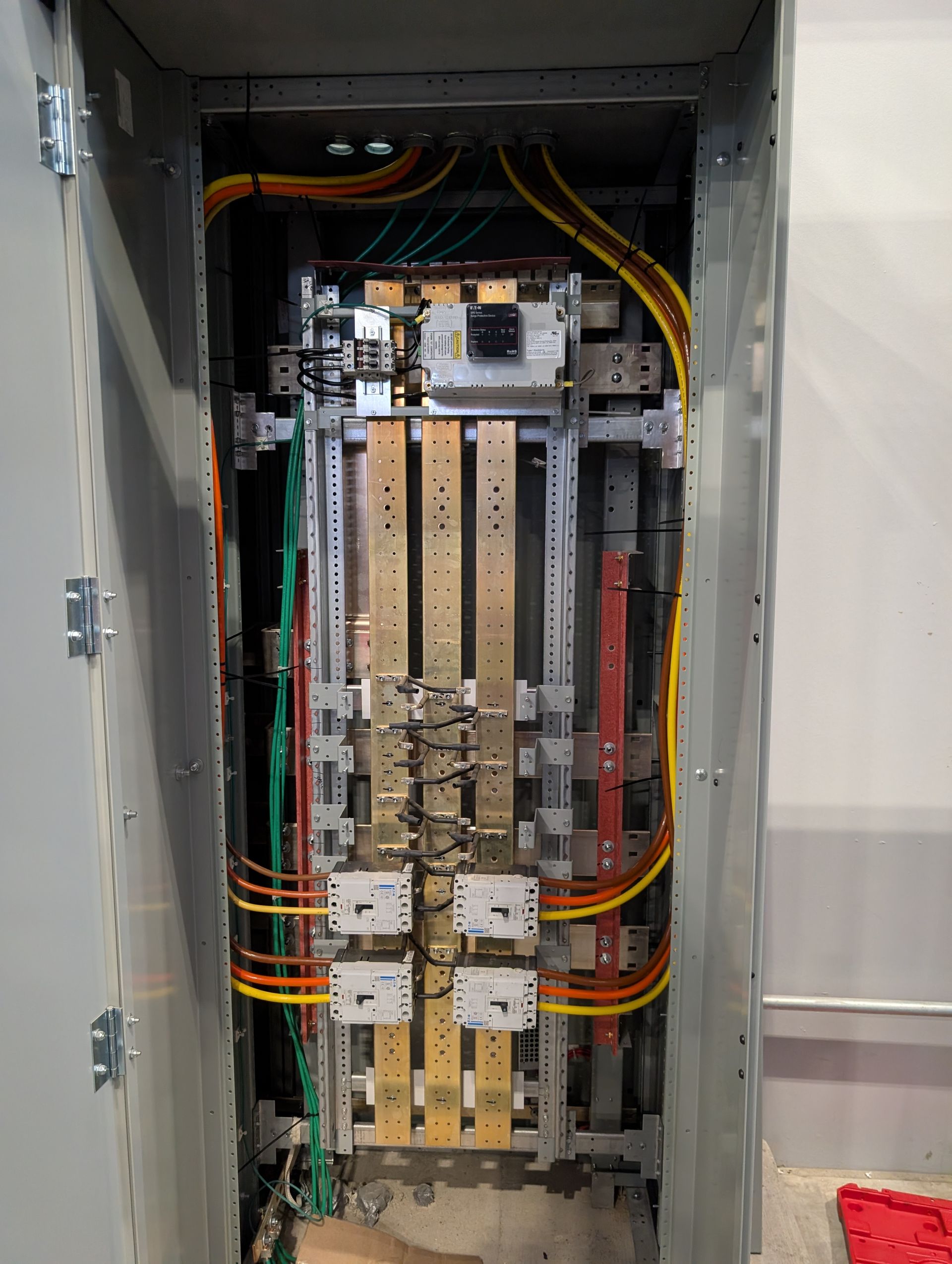 Open electrical panel with rows of circuit breakers and colored wiring inside a wall cabinet