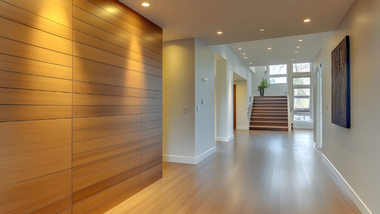 Modern hallway with wood accent wall, light flooring, and stairs leading to a bright entrance.