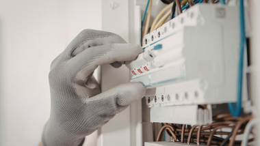 Gloved hand adjusting a circuit breaker panel with wires visible