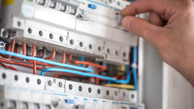 Hand adjusting wires in an electrical breaker panel with red, blue, and white cables