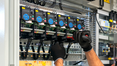 Technician wearing gloves adjusting wiring in an electrical control panel with circuit modules.