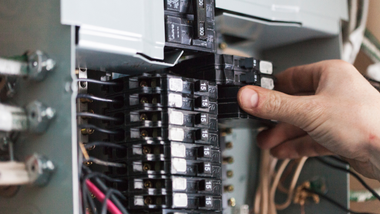 Hand adjusting a circuit breaker panel with rows of switches and visible wiring