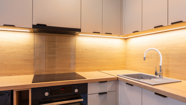 Modern kitchen corner with white cabinets, warm under-cabinet lighting, wooden countertops, stove, and sink