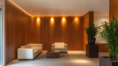 Modern lobby with warm wood walls, white sofas, and potted plants under soft ceiling lights