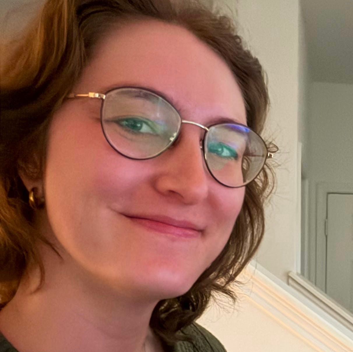A woman in a red sweater is smiling in front of a window.