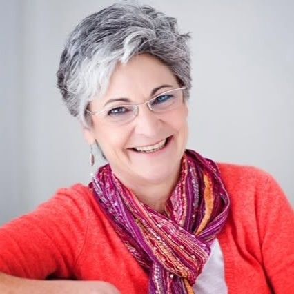 A woman in a red sweater is smiling in front of a window.