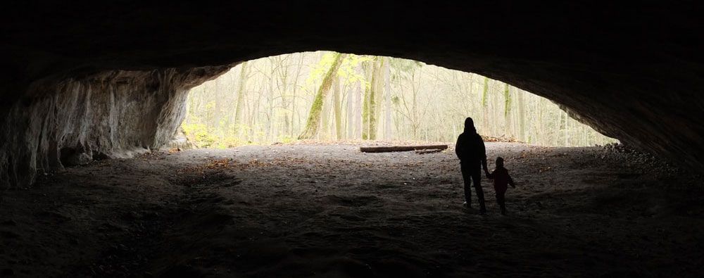 UnimaginableCall A man and a child are standing in a cave holding hands.