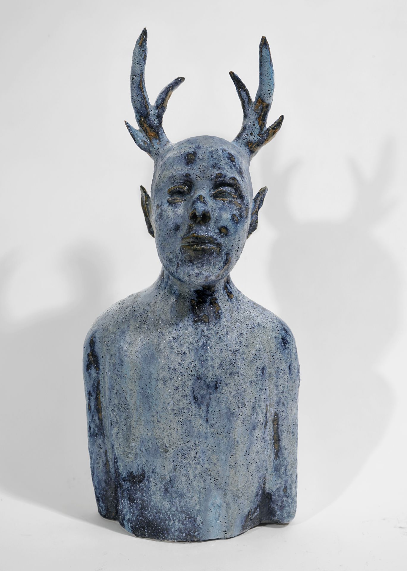 Blue-toned sculpture of a human-like bust with deer antlers.