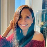 A woman in a red sweater is smiling in front of a window.