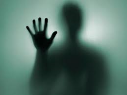 A silhouette of a person behind a frosted glass with their hand up.