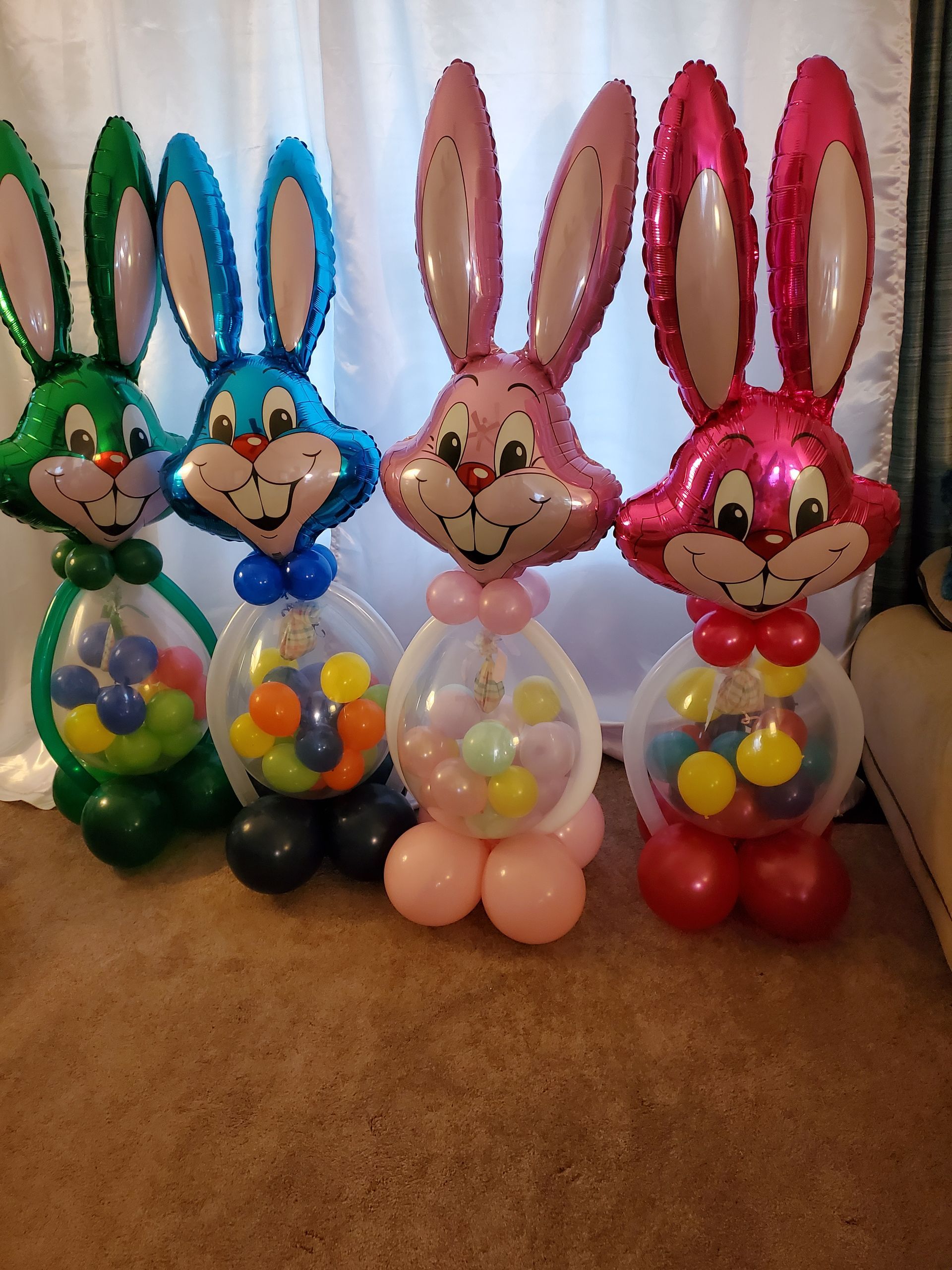 Four balloon sculptures of rabbits in green, blue, pink, and red, each with a clear belly filled with small colored balloons.