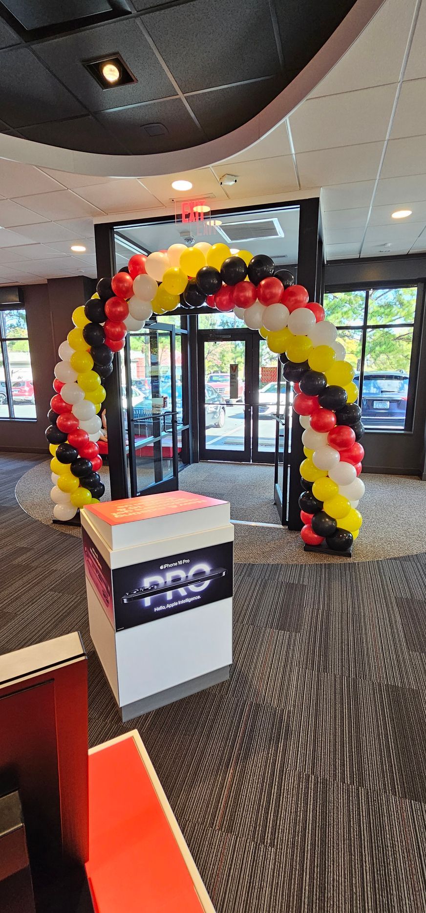 An arch made of black, white, red, and yellow balloons stands at a doorway inside a building.