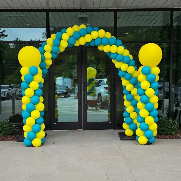 Yellow and teal balloon arch over glass doors, flanked by columns of balloons.