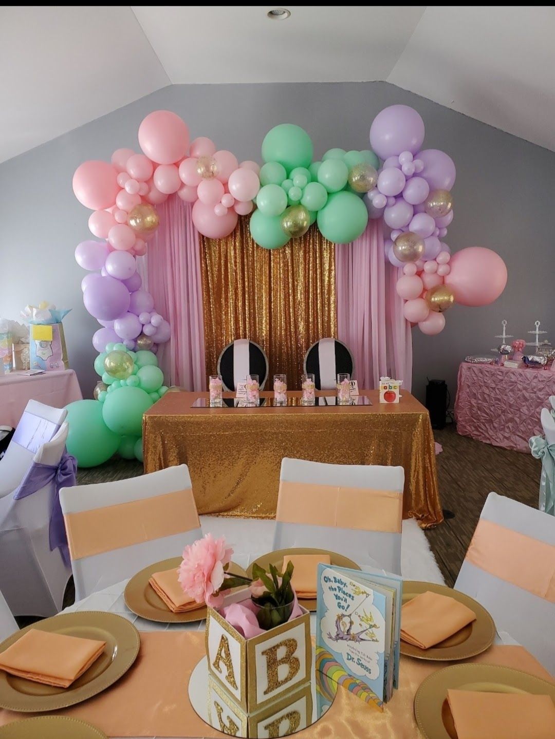 Decorated table with gold sequin cloth and a balloon arch in pink, green, and lavender for a baby shower or event.